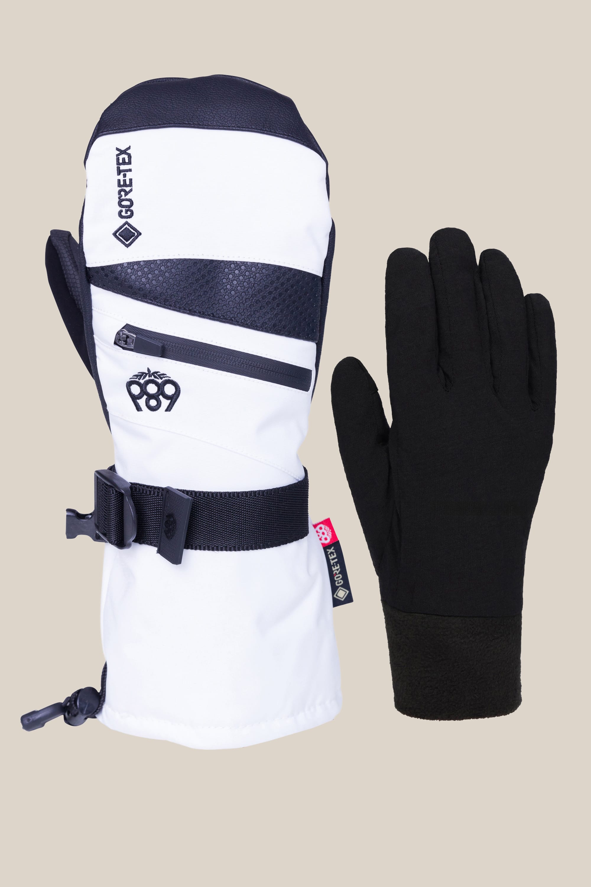 The 686 Womens GORE-TEX Smarty 3-In-1 Gauntlet Mitt by 686 is shown in black-and-white PU with zippers and an adjustable strap, alongside a plain black glove liner, both set on a light beige background.