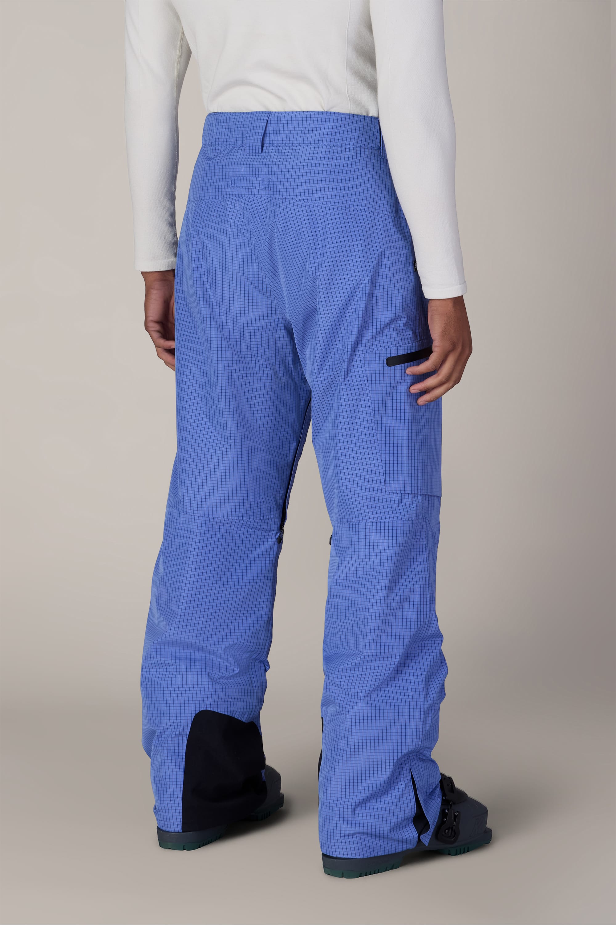 A person is shown from the back, standing against a plain light background, wearing 686 Men’s Hydra™ Thermagraph® Pant by 686 in blue, a white long-sleeve top, and black boots.