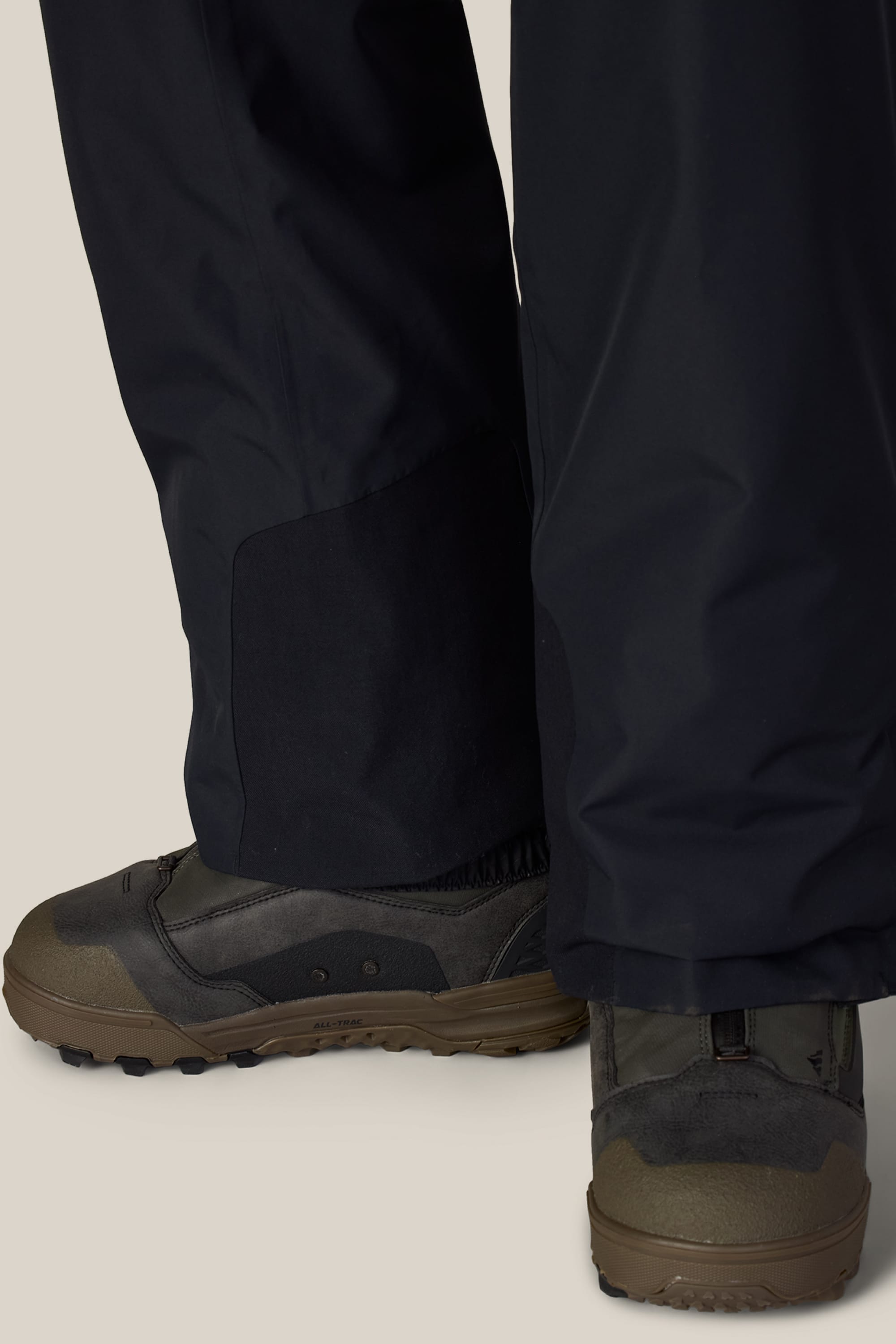 Close-up of a person wearing 686 Men’s Hydra™ Thermagraph® Pant and brown hiking boots, standing on a light-colored surface. Only the lower legs and feet are visible.