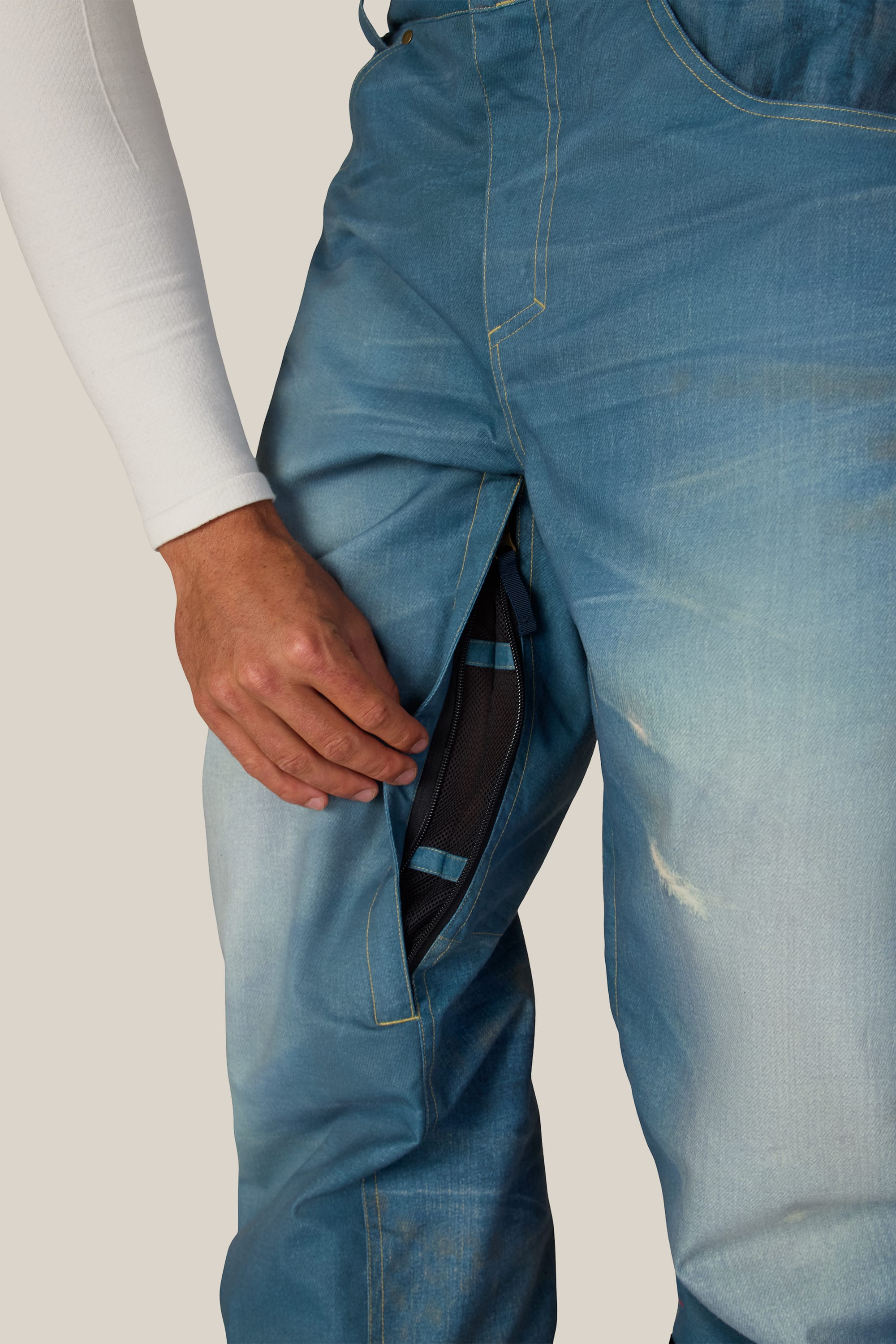 A person wearing the 686 Men’s Deconstructed™ Denim Insulated Pant and a white sleeve opens a mesh-lined zippered vent on the upper thigh of the pants.