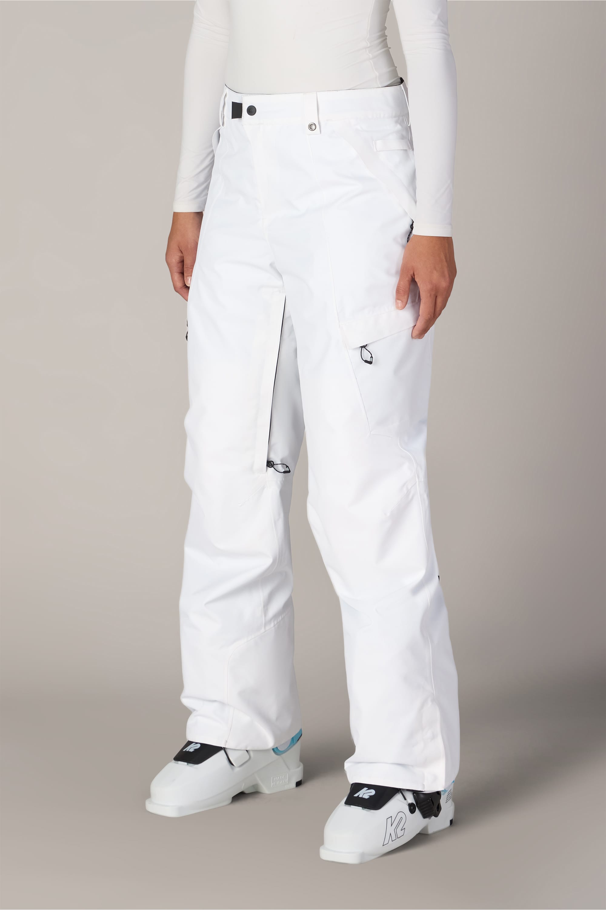 A person is shown from the waist down, standing against a neutral background, wearing the 686 Women’s Geode Thermagraph® Pant in white along with a matching white long-sleeve top and white ski boots.