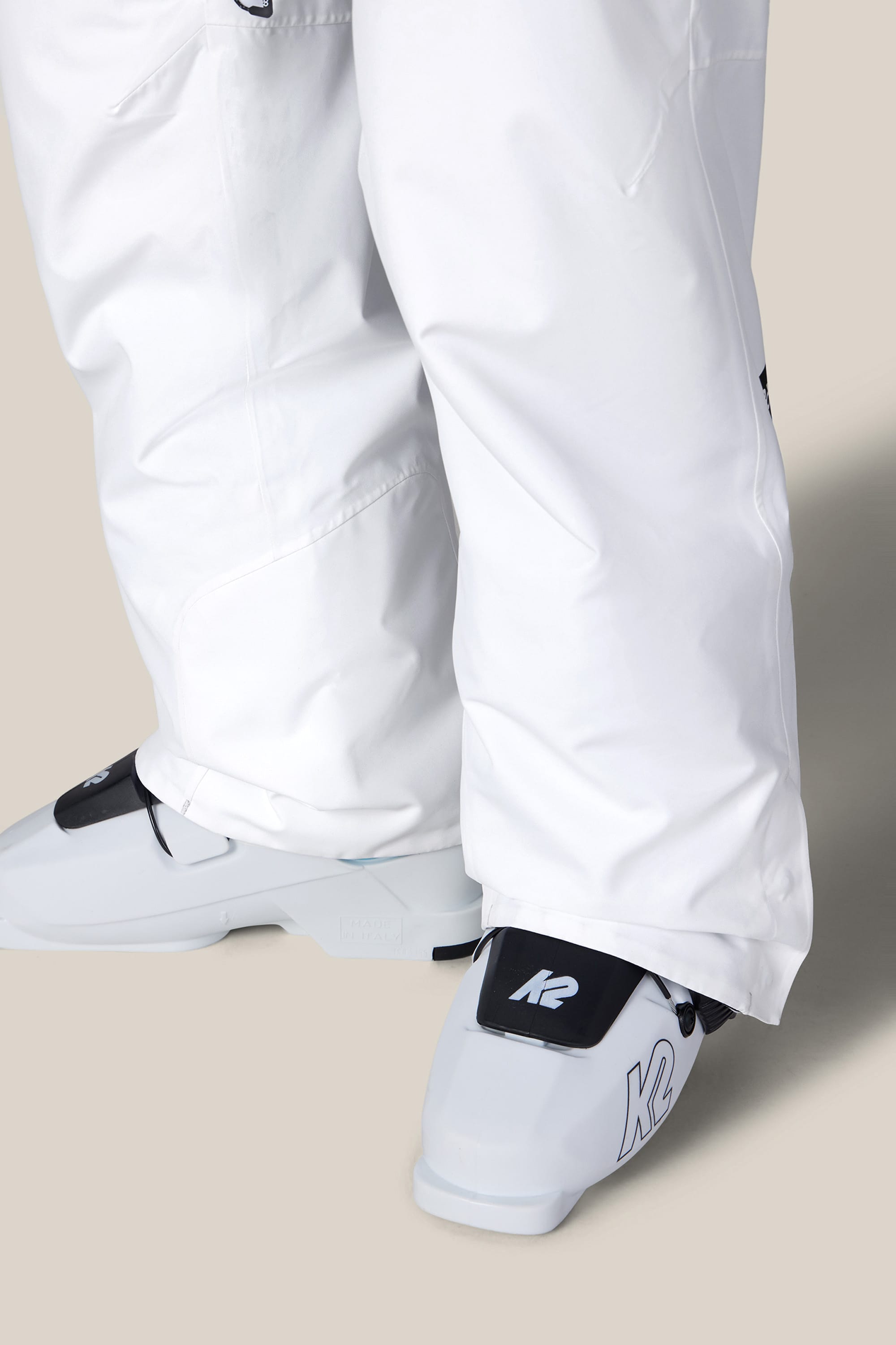 A person wearing 686 Women’s Geode Thermagraph® Pant in white and white K2 ski boots stands on a beige surface.