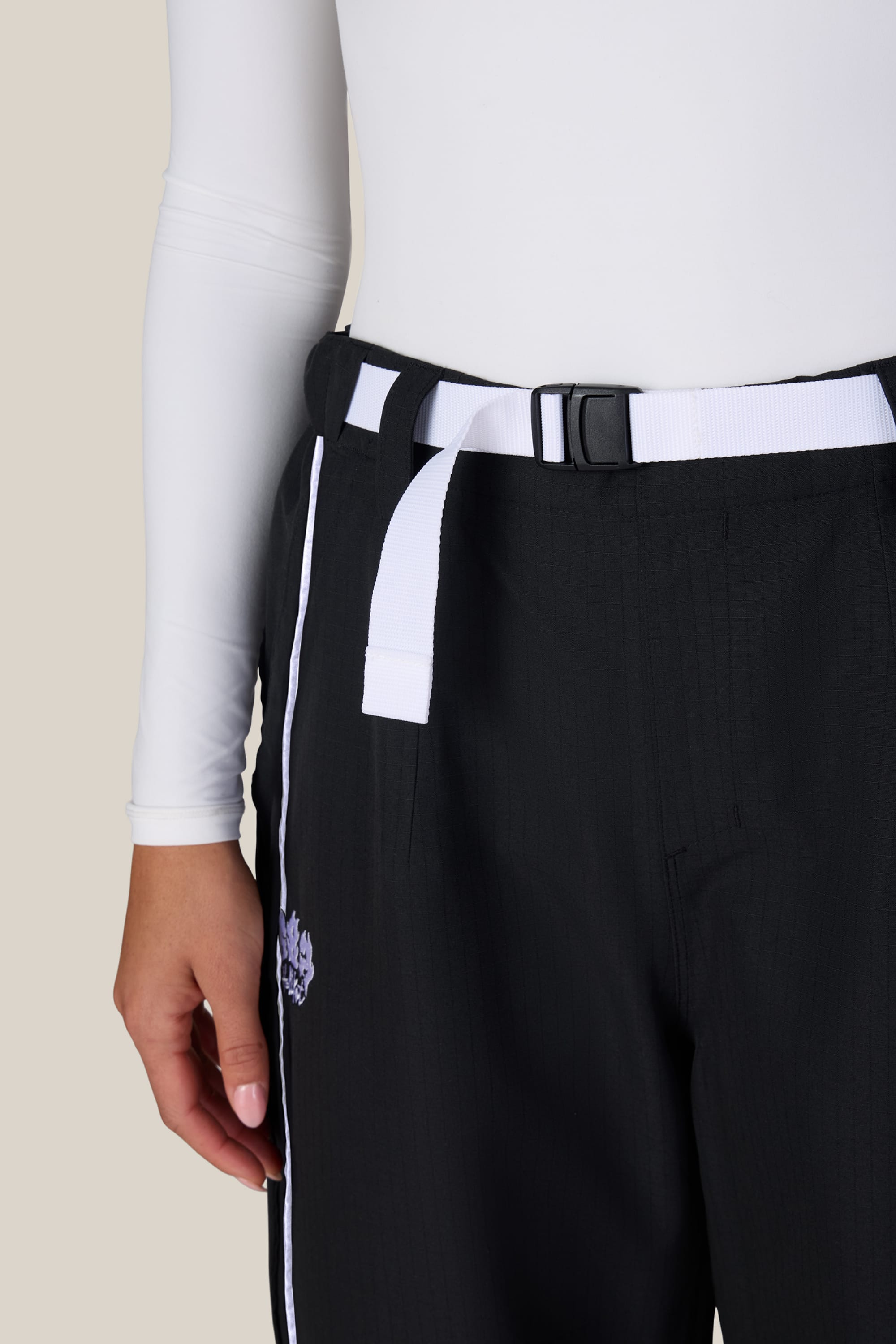 A person wearing 686 Women’s Hellkat™ Shell Pant with a white side stripe and a white belt, paired with a fitted white long-sleeve top. Only the lower torso and one arm are visible.