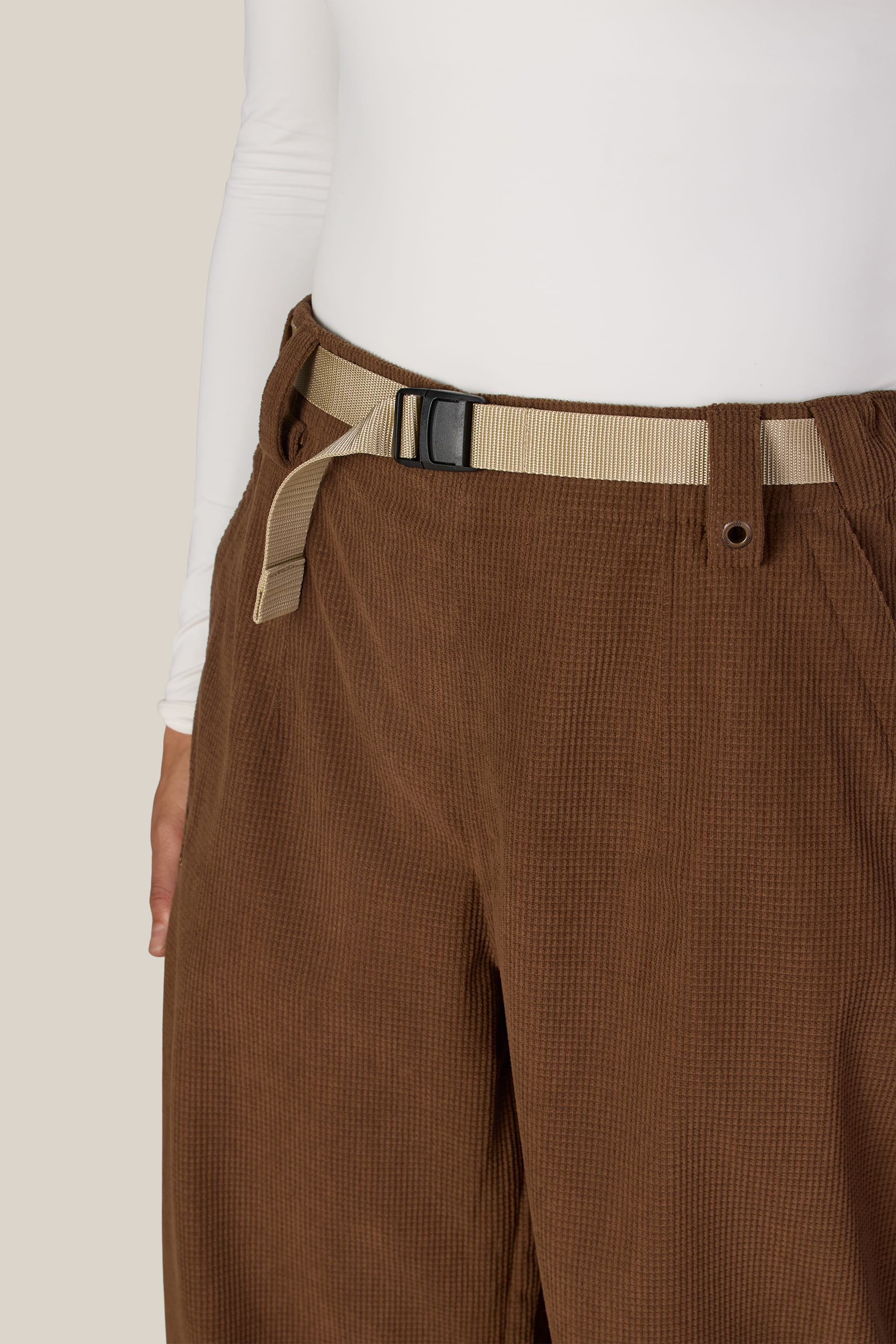 A person wearing the 686 Women’s Hellkat™ Shell Pant in brown, styled with a beige webbing belt and a white long-sleeve top, shown from the waist down against a light background.