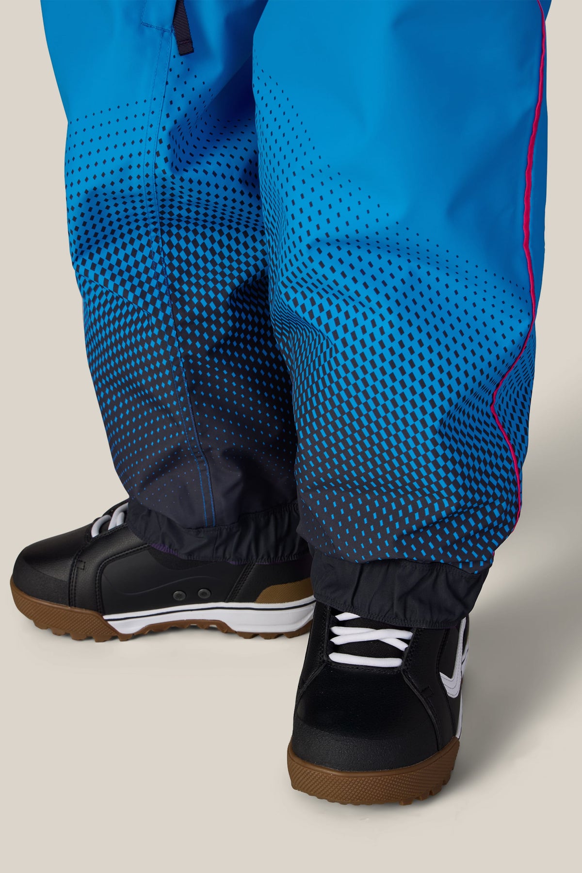 Close-up of a person wearing 686 Women’s Fox Racing 97 Shell Pants in blue with a black geometric gradient pattern and black snow boots.