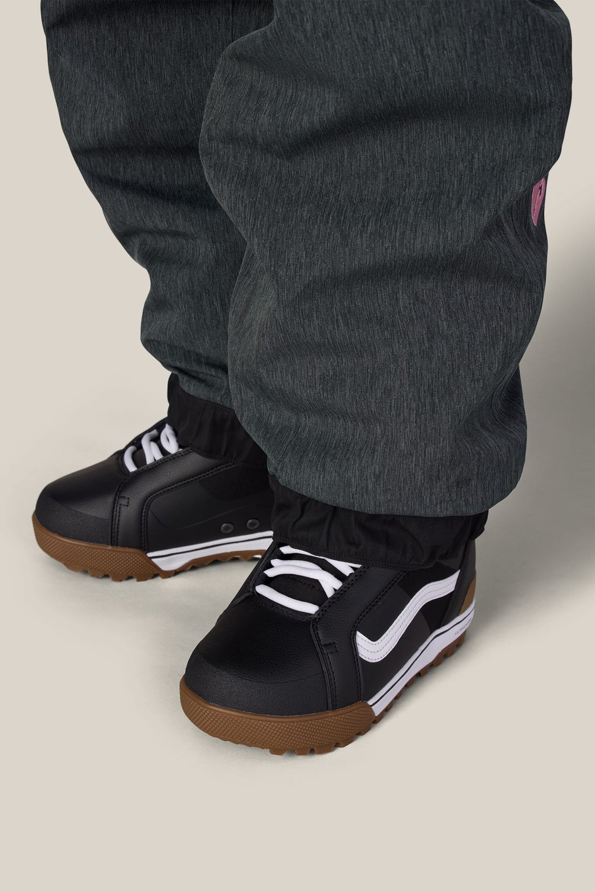 A person wearing charcoal grey 686 Women’s Metallica Burning Skull Shell Pants tucked into black sneakers with white laces and gum-colored soles.