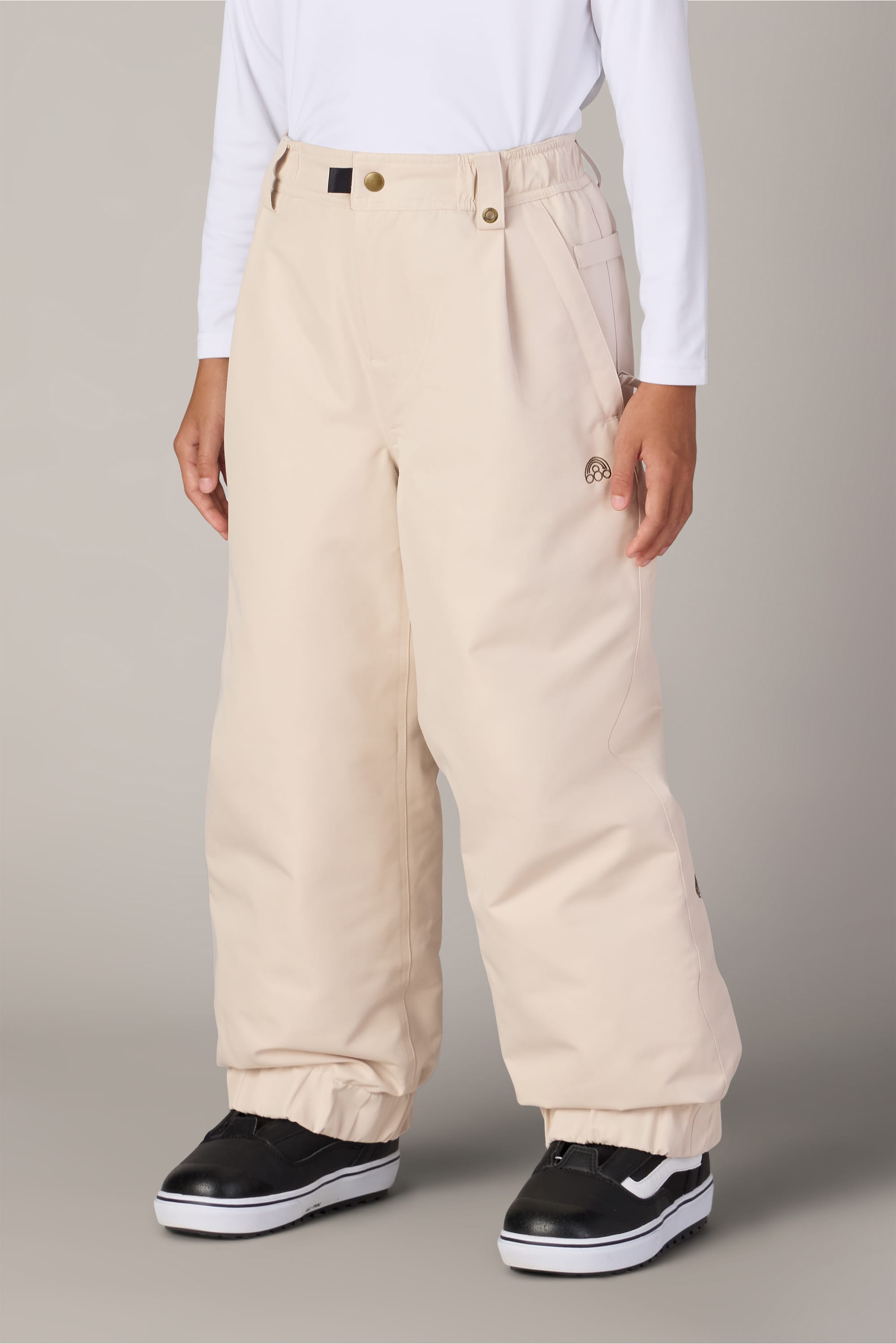 A person is wearing the 686 Girls’ Outline™ Insulated Pant by 686, along with a long-sleeve white shirt and black-and-white skate shoes, standing against a plain gray background. Their hands are relaxed at their sides and their face is not visible.