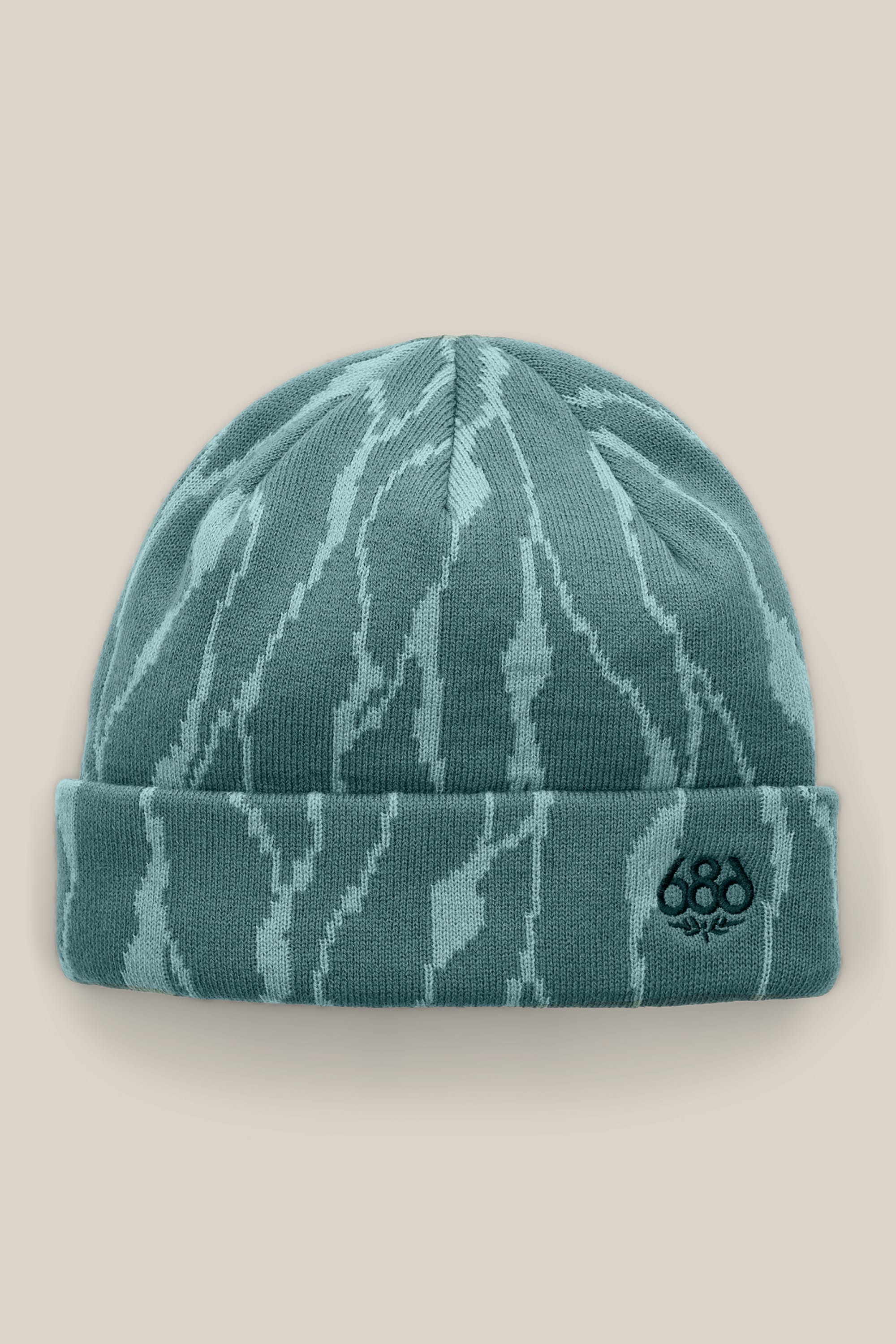 The 686 Women’s Cepa Beanie features a teal acrylic knit design with light blue abstract patterns and a small embroidered 686 logo on the front cuff, shown against a beige background. This stylish beanie by 686 offers women both warmth and modern flair.
