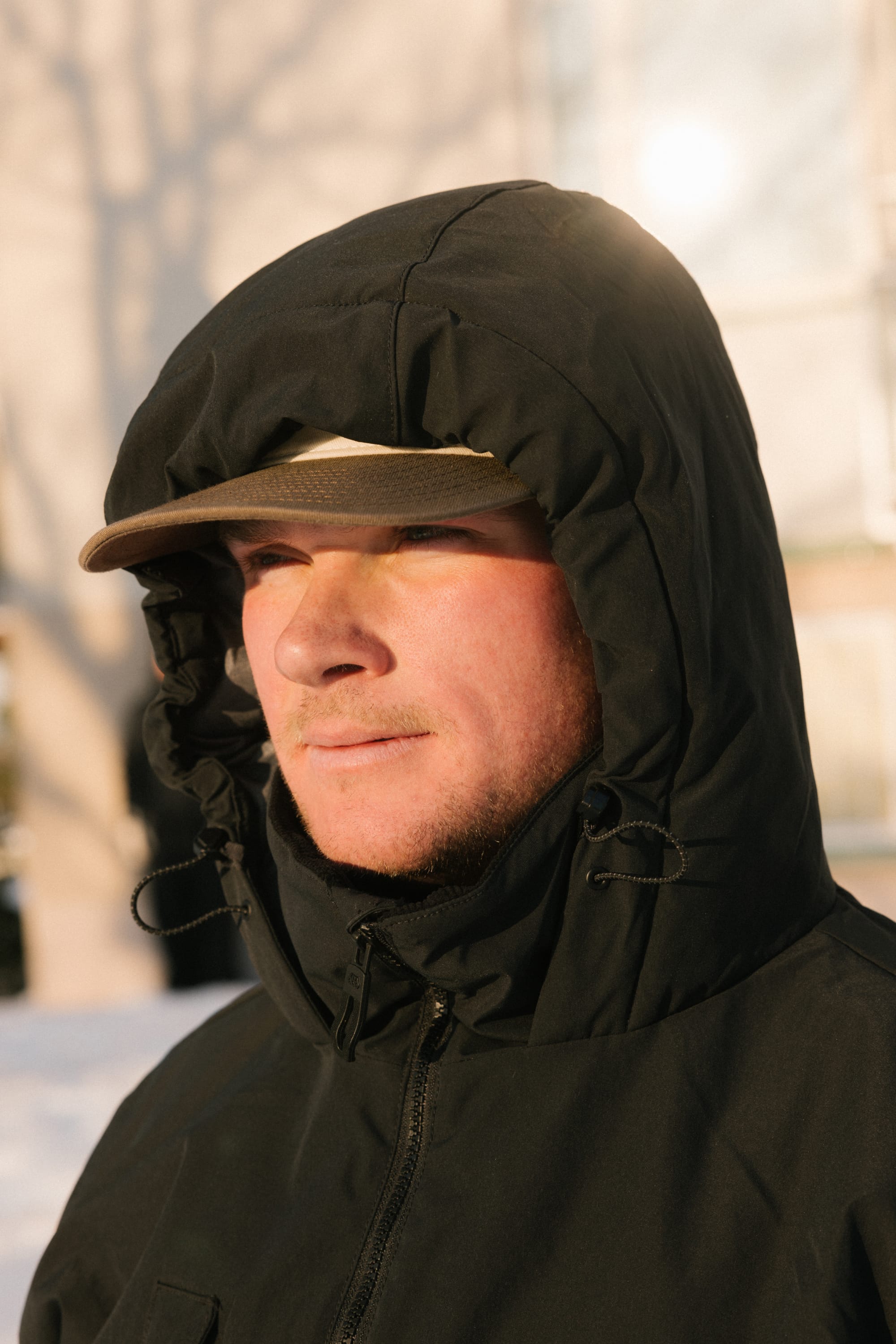 A person wearing the 686 Men’s WINDSTOPPER® Guideline Insulated Jacket by GORE-TEX® LABS and a tan cap stands outside in sunlight, looking off into the distance.