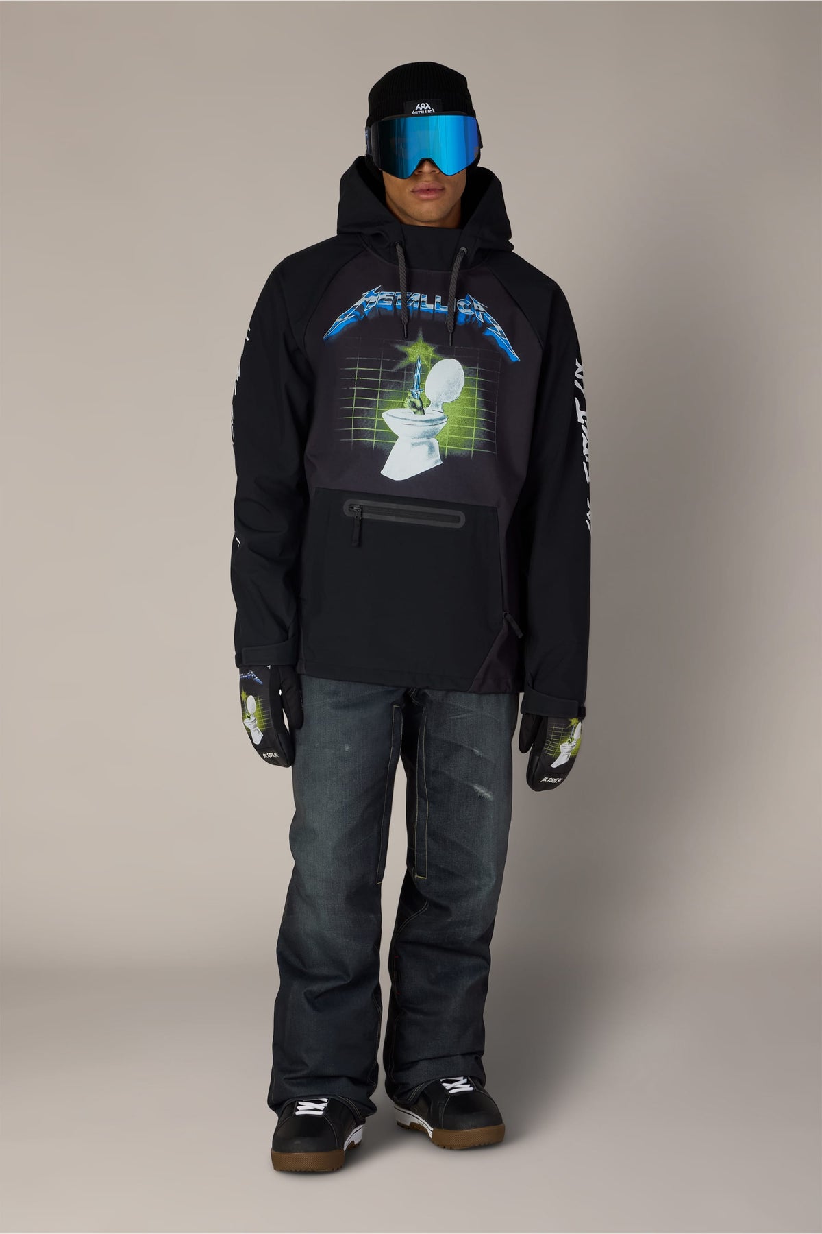 A person wears a black 686 Men’s Metallica Waterproof Hoody with a toilet graphic, paired with dark jeans, a beanie, reflective goggles, and matching gloves.