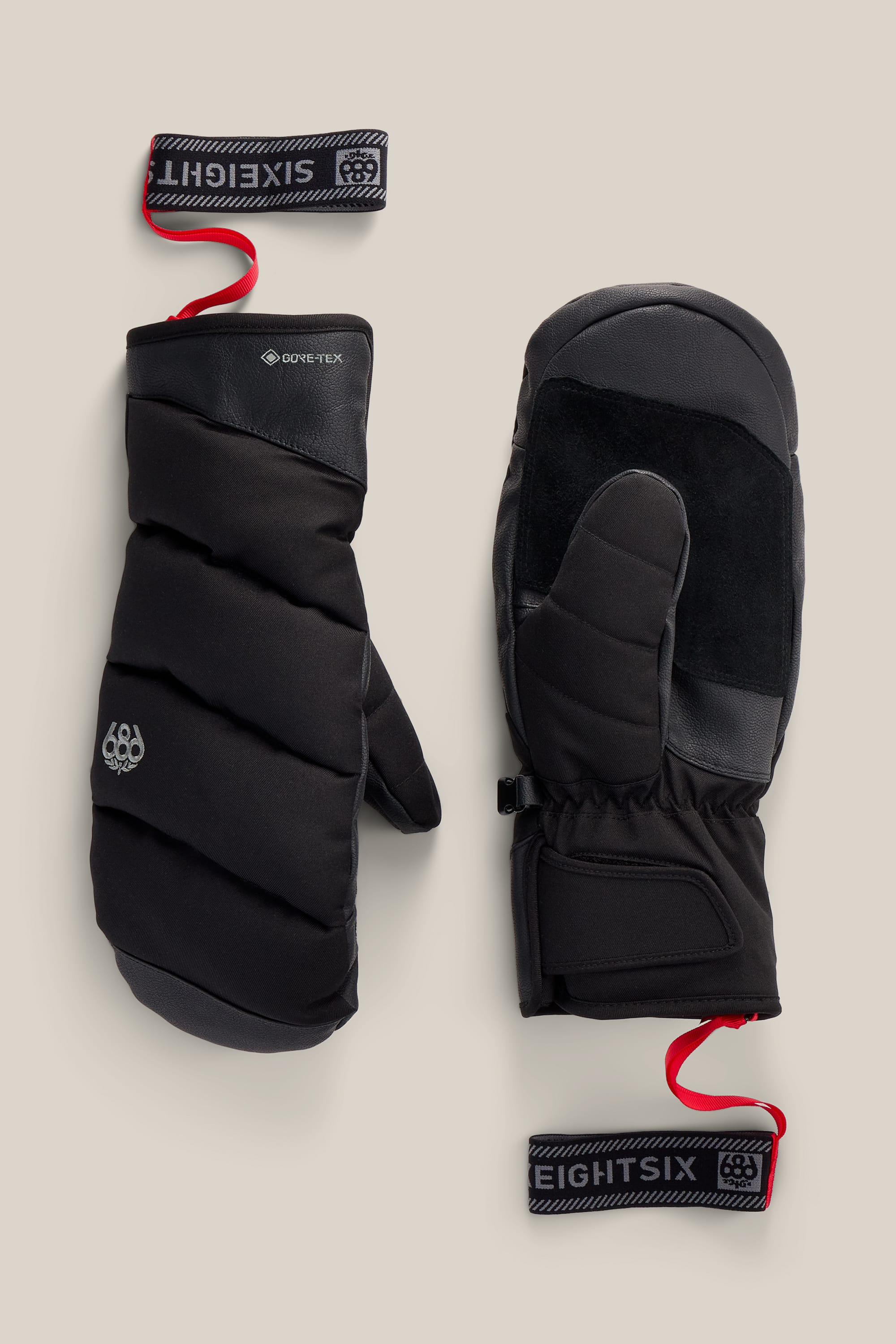 A pair of 686 Men’s GORE-TEX® Buffer Insulated Mitts in black, featuring red wrist straps. The left mitten displays the back with the GORE-TEX logo, while the right showcases the poly mitt palm and thumb. Both mitts are equipped with velcro wrist straps labeled EIGHTSIX and SIXEIGHT.