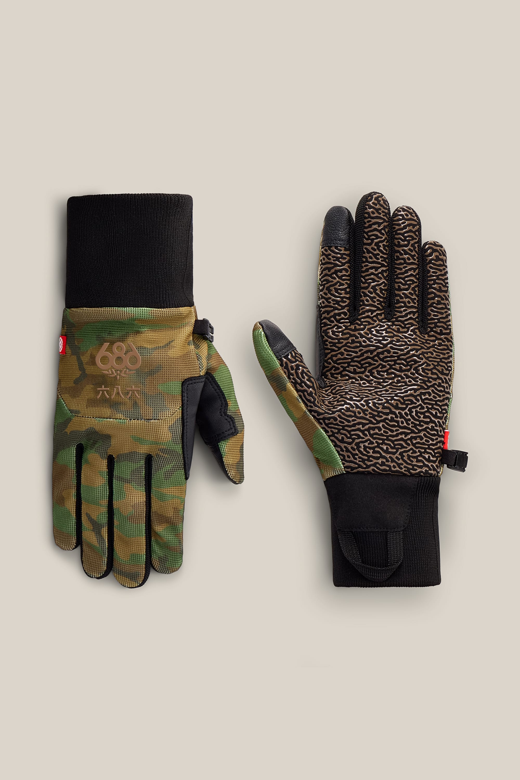 A pair of 686 Men’s Hold Up Pipe Gloves: one palm-up reveals a textured brown and black PU grip, while the other shows a green camouflage pattern with the 686 logo; both feature black cuffs and are displayed on a beige background.