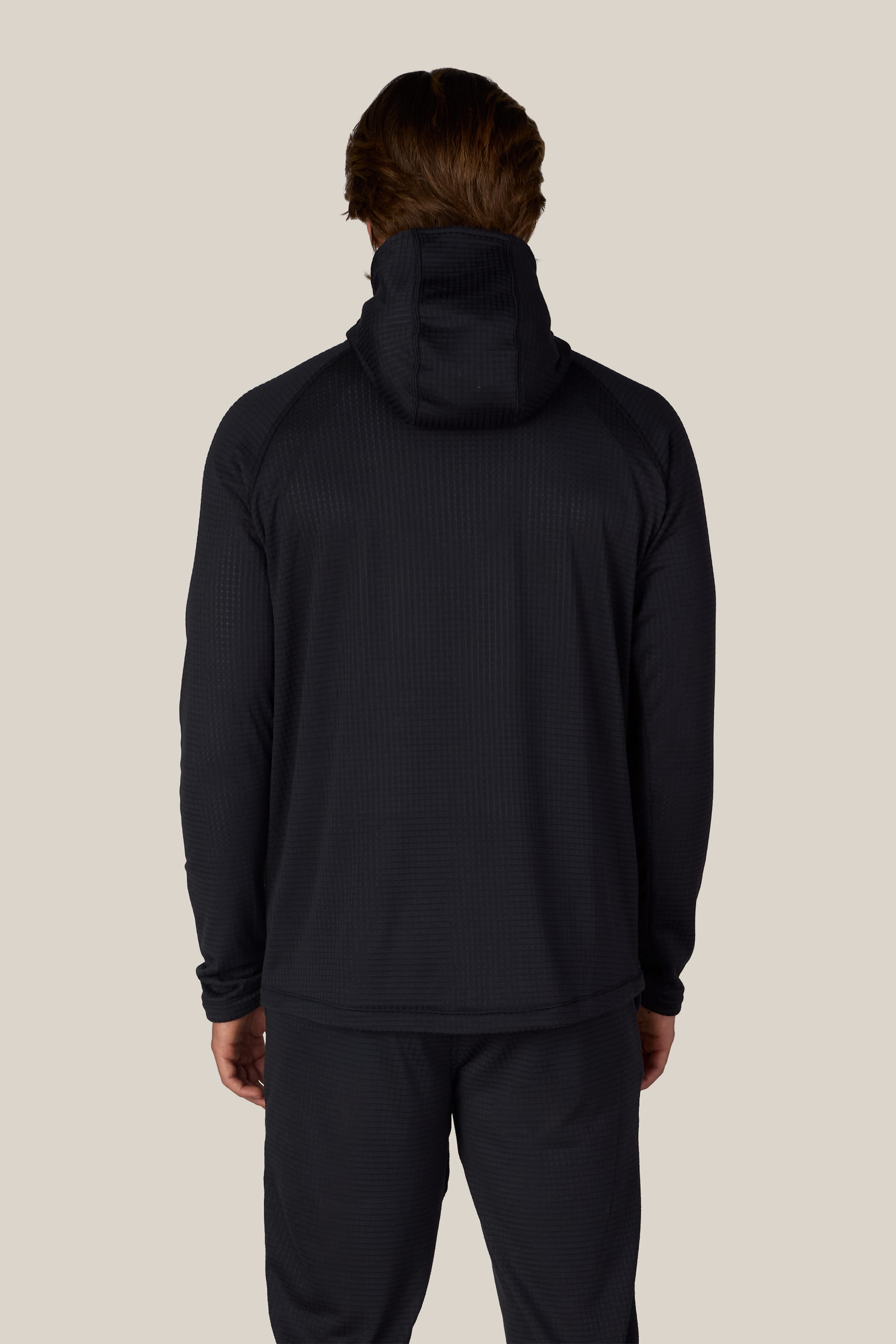 A person is standing facing away, showcasing the back view of the outfit against a plain light background while wearing black pants and the 686 Men’s Mission Grid™ Raglan Hoody by 686.