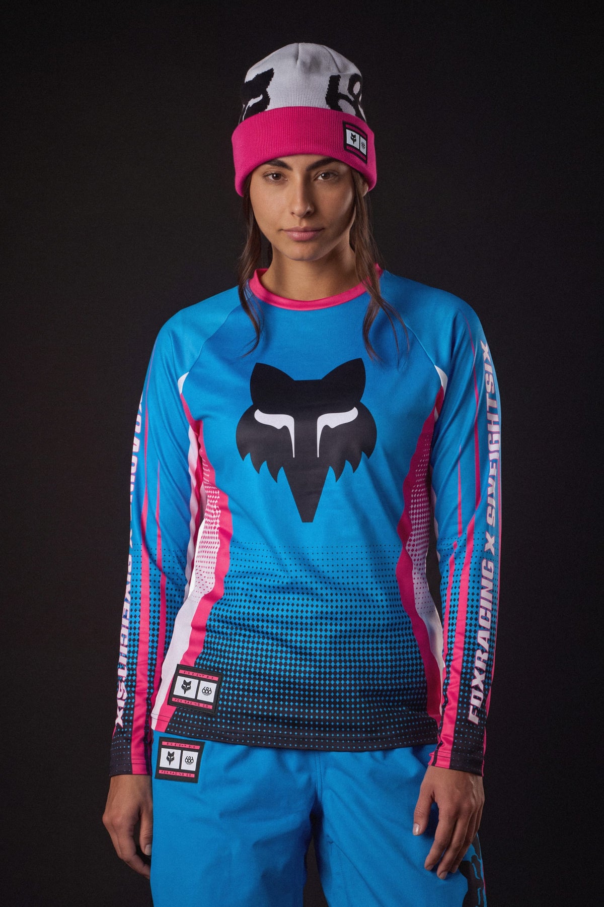 A woman wearing a white and pink beanie and a 686 Women’s Fox Racing Base Layer LS.
