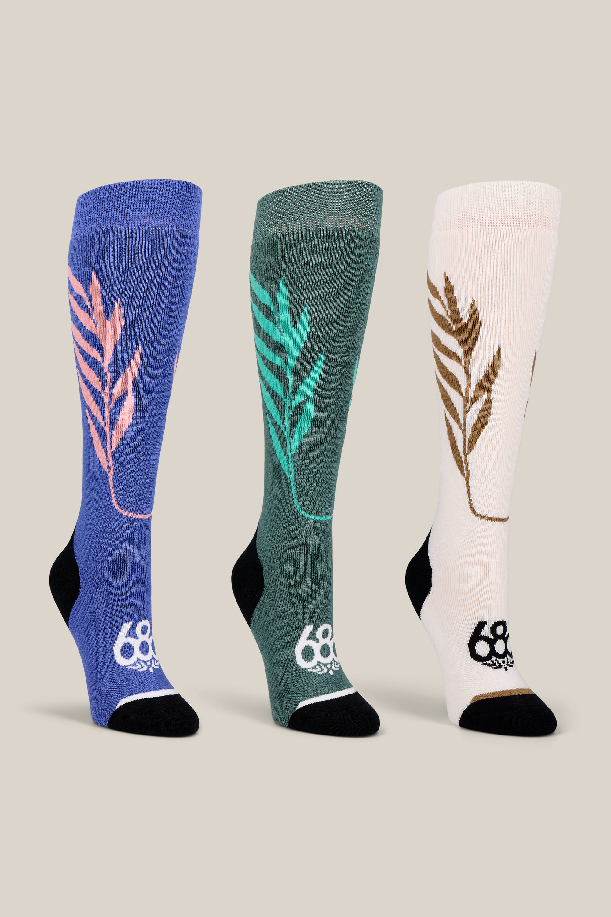 The 686 Women’s Willow Socks - 3-Pack includes three knee-high socks in blue, green, and white, each accented with a colored leaf pattern along the side and the 686 logo near the toe. Designed for performance, these socks feature black heels and toes to enhance durability and comfort.
