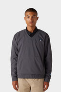 A person stands facing forward wearing the 686 x Malbon Mens PrimaLoft drirelease® Merino-Lined Pullover Jacket in dark grey with a small chest logo, paired with light khaki pants against a plain light background.
