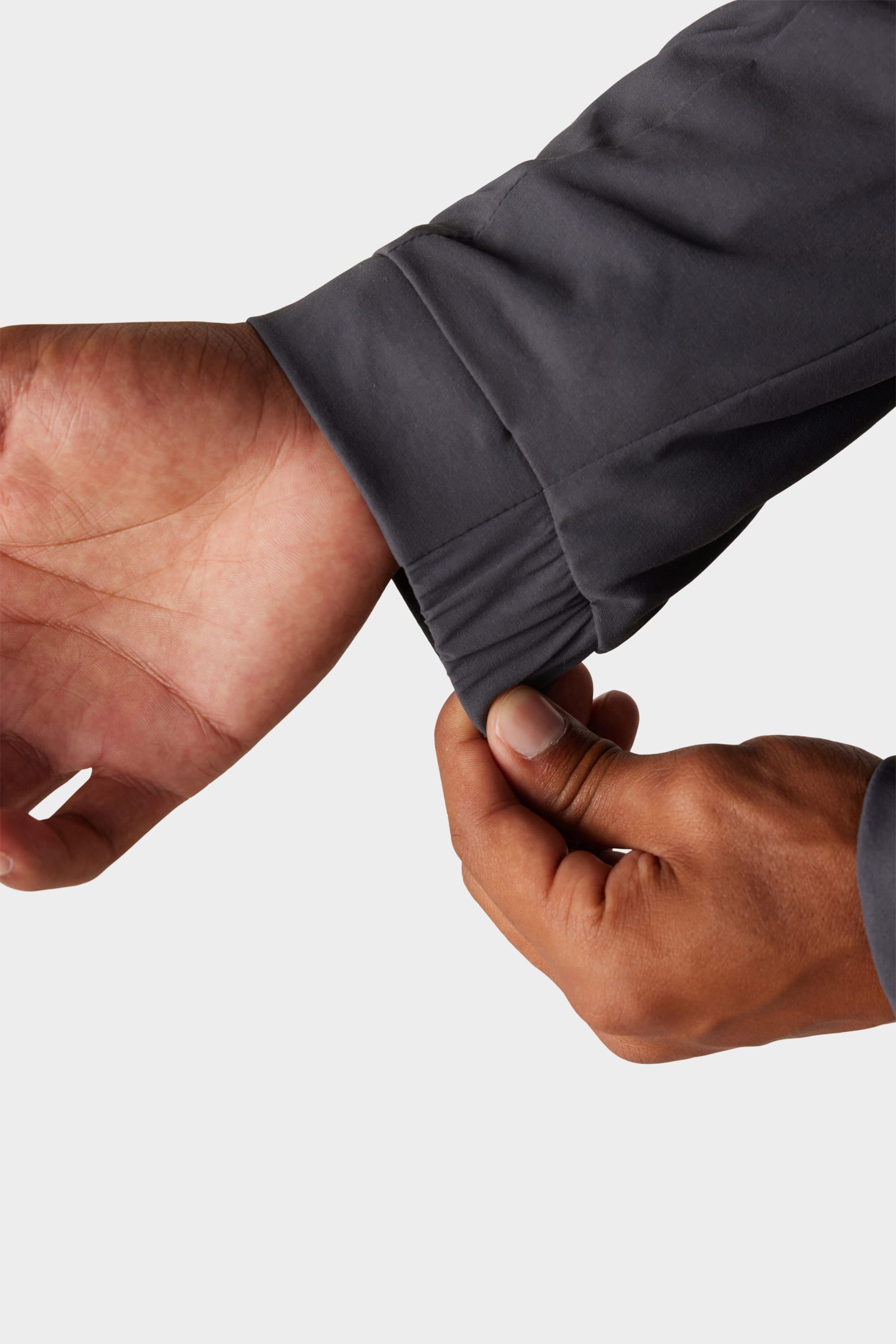A person adjusts the cuff of a 686 x Malbon Mens PrimaLoft drirelease® Merino-Lined Pullover Jacket, with a close-up of the wrist and sleeve set against a plain light background.