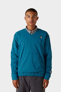 A person stands facing forward, wearing the 686 x Malbon Mens PrimaLoft drirelease® Merino-Lined Pullover Jacket over a grey collared shirt and dark pants, set against a plain light background.