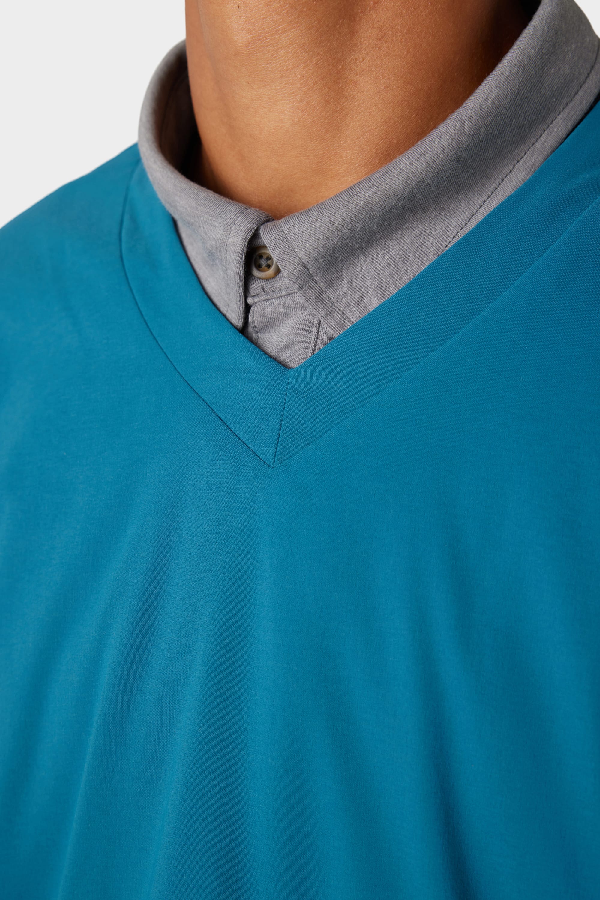 Close-up of a person wearing the 686 x Malbon Mens PrimaLoft drirelease® Merino-Lined Pullover Jacket in blue over a light grey shirt; only the neckline and upper chest are visible, not the face.