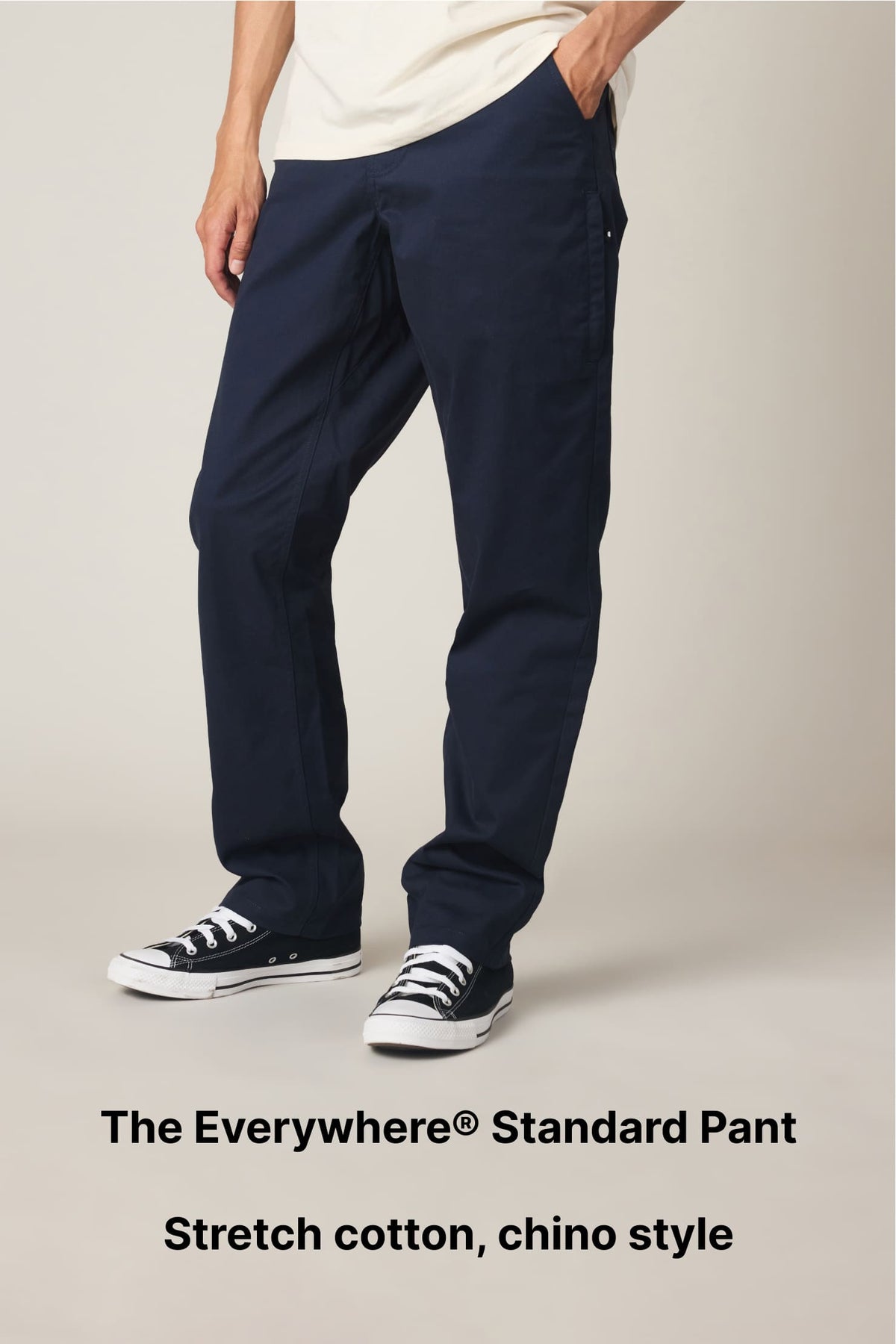 Person wearing navy blue chino-style pants and black sneakers with white soles, standing against a plain background. Text reads: The Everywhere® Standard Pant. Stretch cotton, chino style..