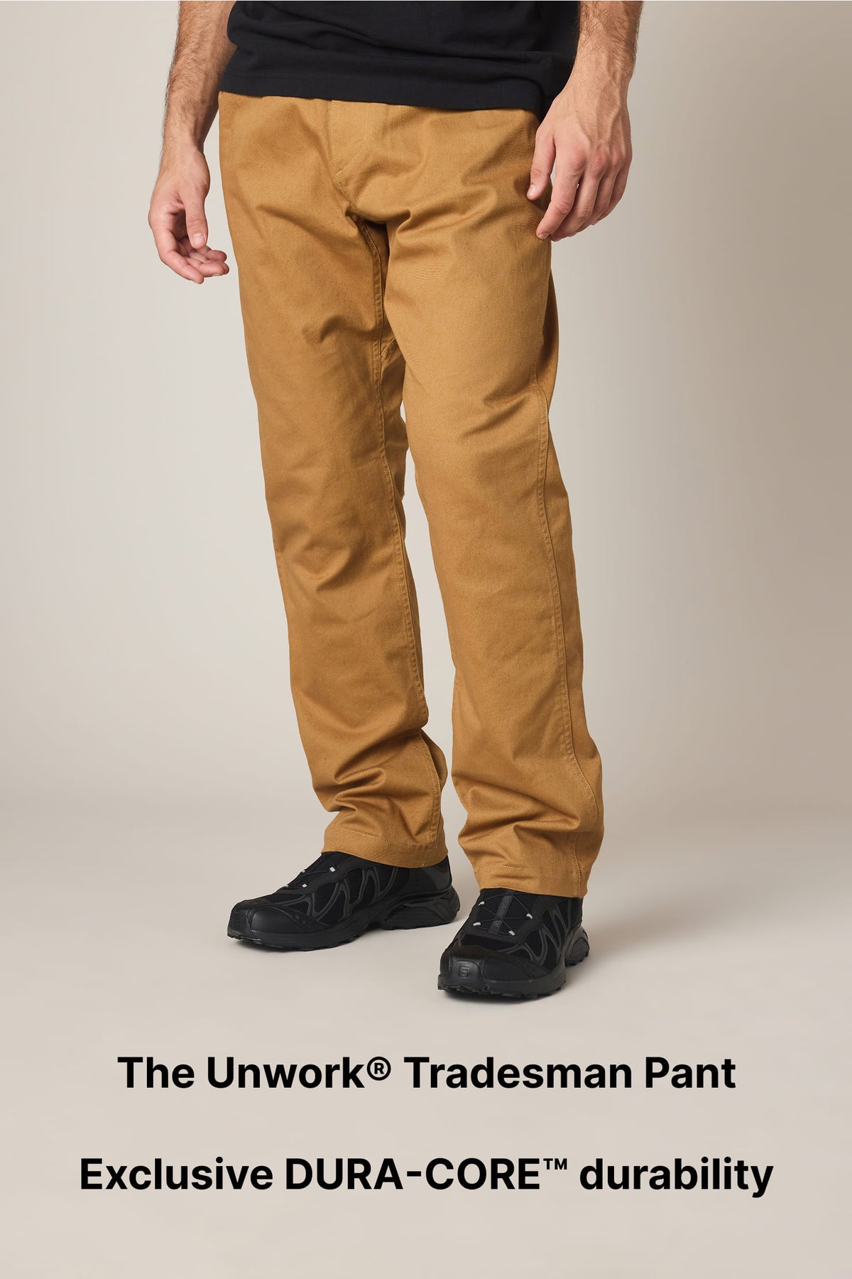 A person wearing tan work pants and black shoes stands against a plain background. Text below reads: The Unwork® Tradesman Pant. Exclusive DURA-CORE™ durability..