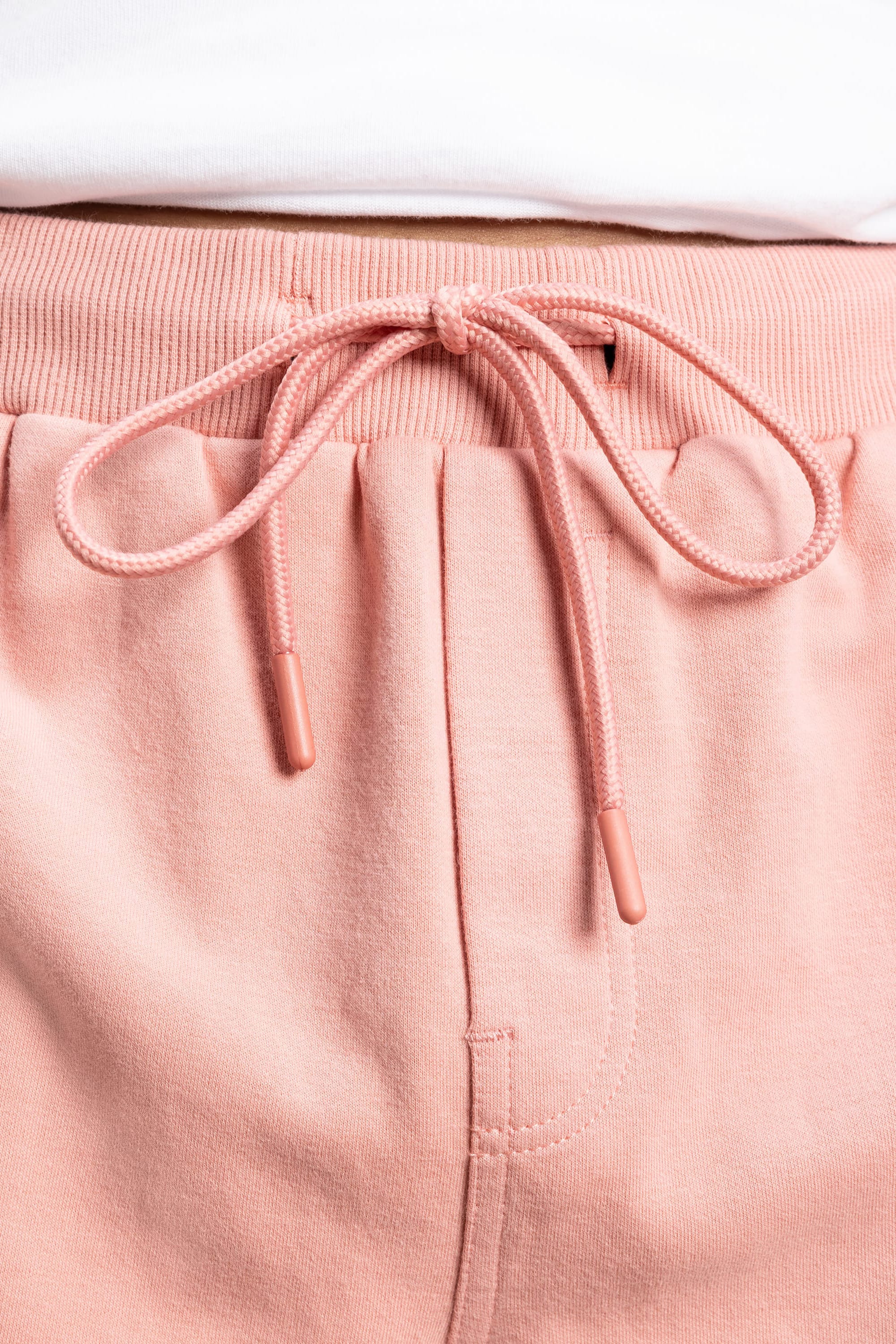 Close-up of 686 Mens Everywhere Double Knit Shorts in light pink with a drawstring waistband, showing the tied drawstring and part of a white shirt above. Brand: 686.