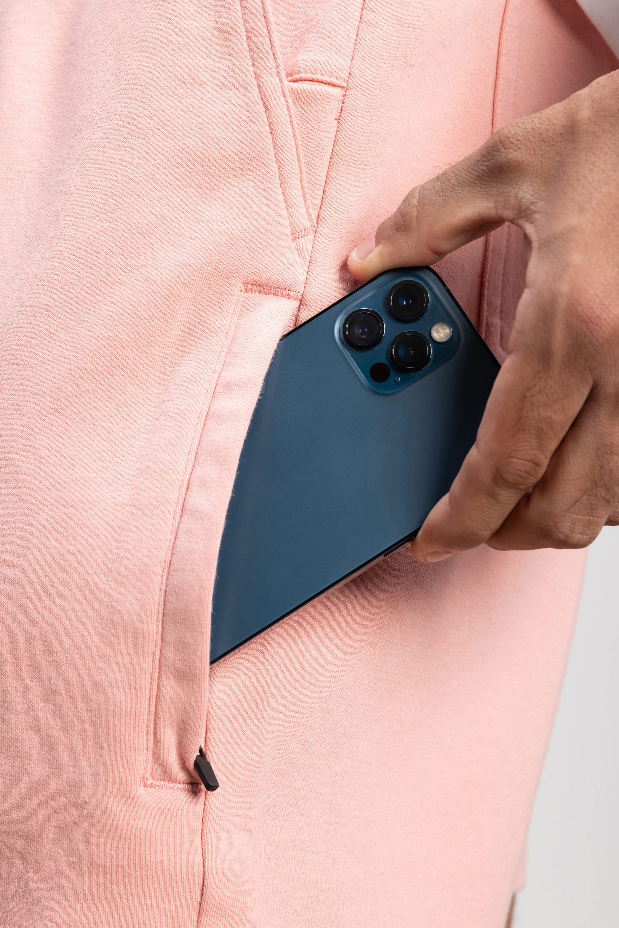 A person’s hand is placing a dark blue smartphone with three rear cameras into the pocket of 686 Mens Everywhere Double Knit Short by 686.
