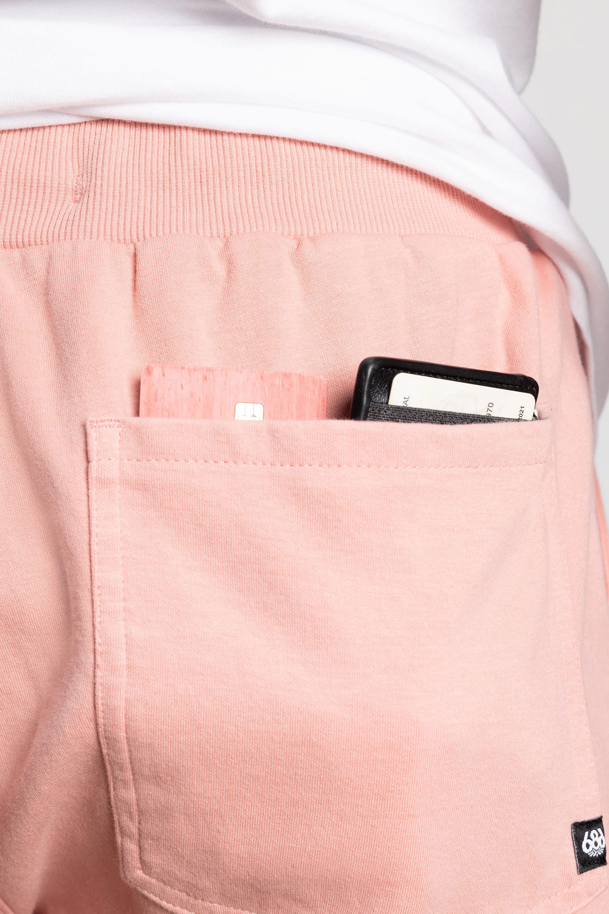 A close-up of the back pocket of 686 Mens Everywhere Double Knit Short by 686, holding a phone with a visible SIM card and a card with text, worn by someone in a white shirt.