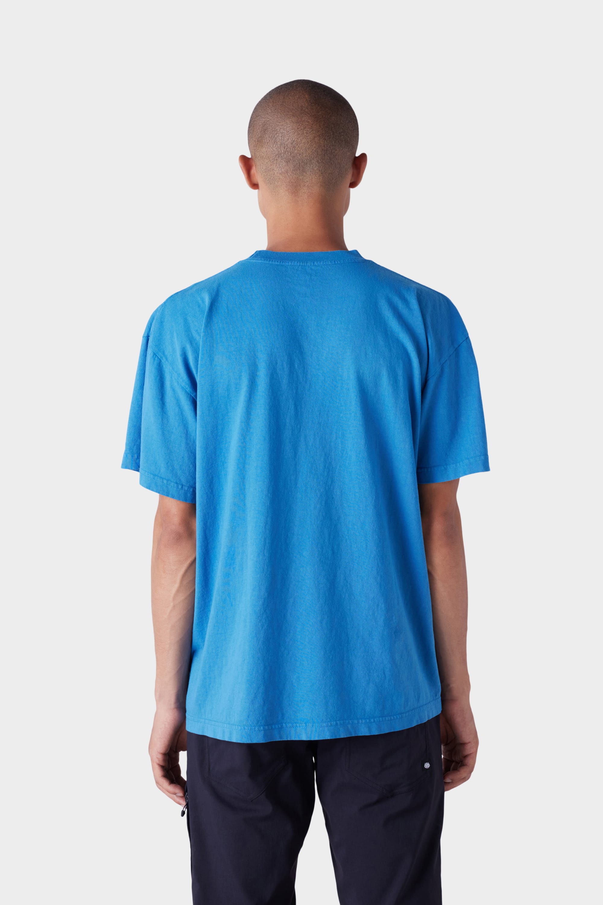 A person with a shaved head is shown from behind, wearing the 686 Mens Wreath Short Sleeve Tee in bright blue and dark pants against a plain light background.