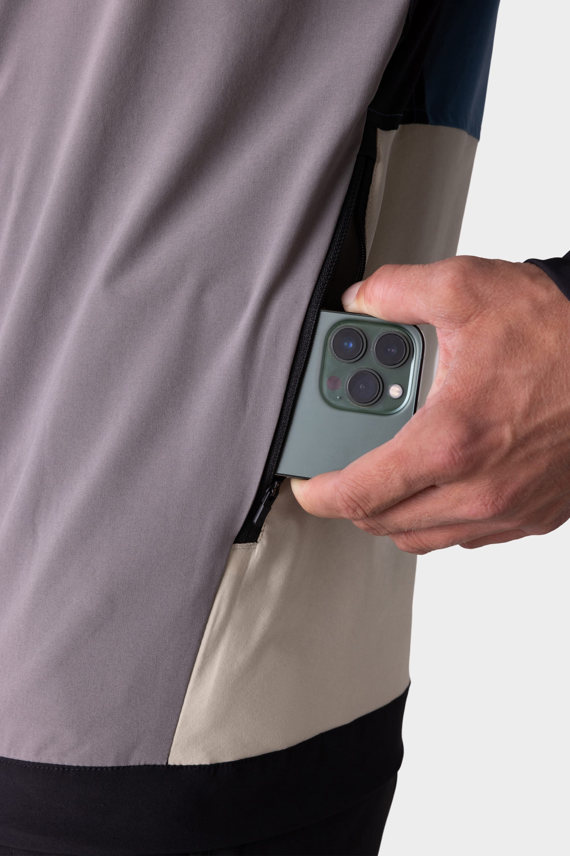 A hand slips a three-camera smartphone into the zippered side pocket of the 686 Mens ATP Stretch Wind Jacket, a color-blocked 686 jacket in gray, beige, and black.