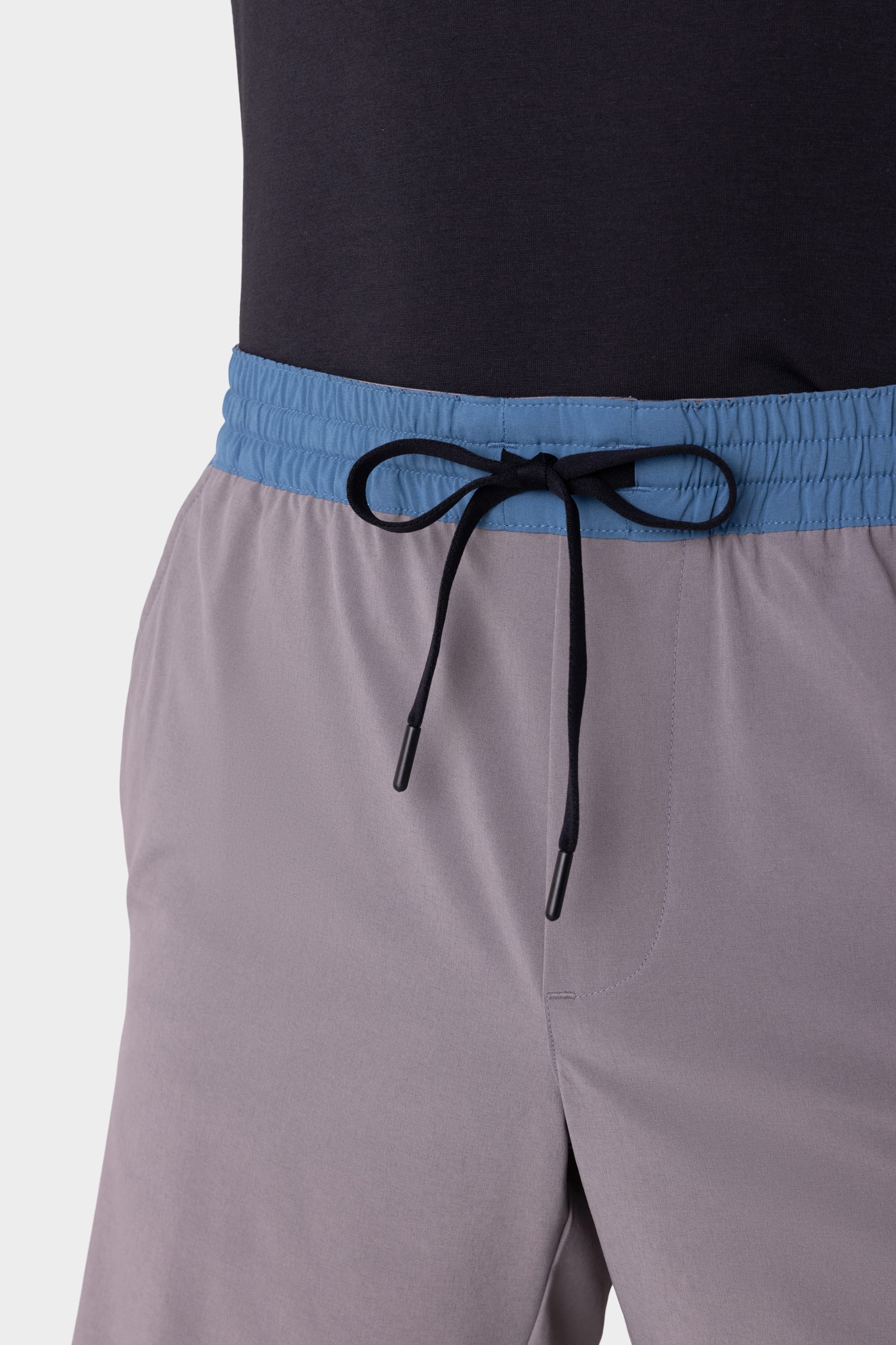 Close-up of a person wearing the 686 Mens ATP Stretch Performance Short in light gray with a blue waistband and black drawstring, paired with a dark shirt.
