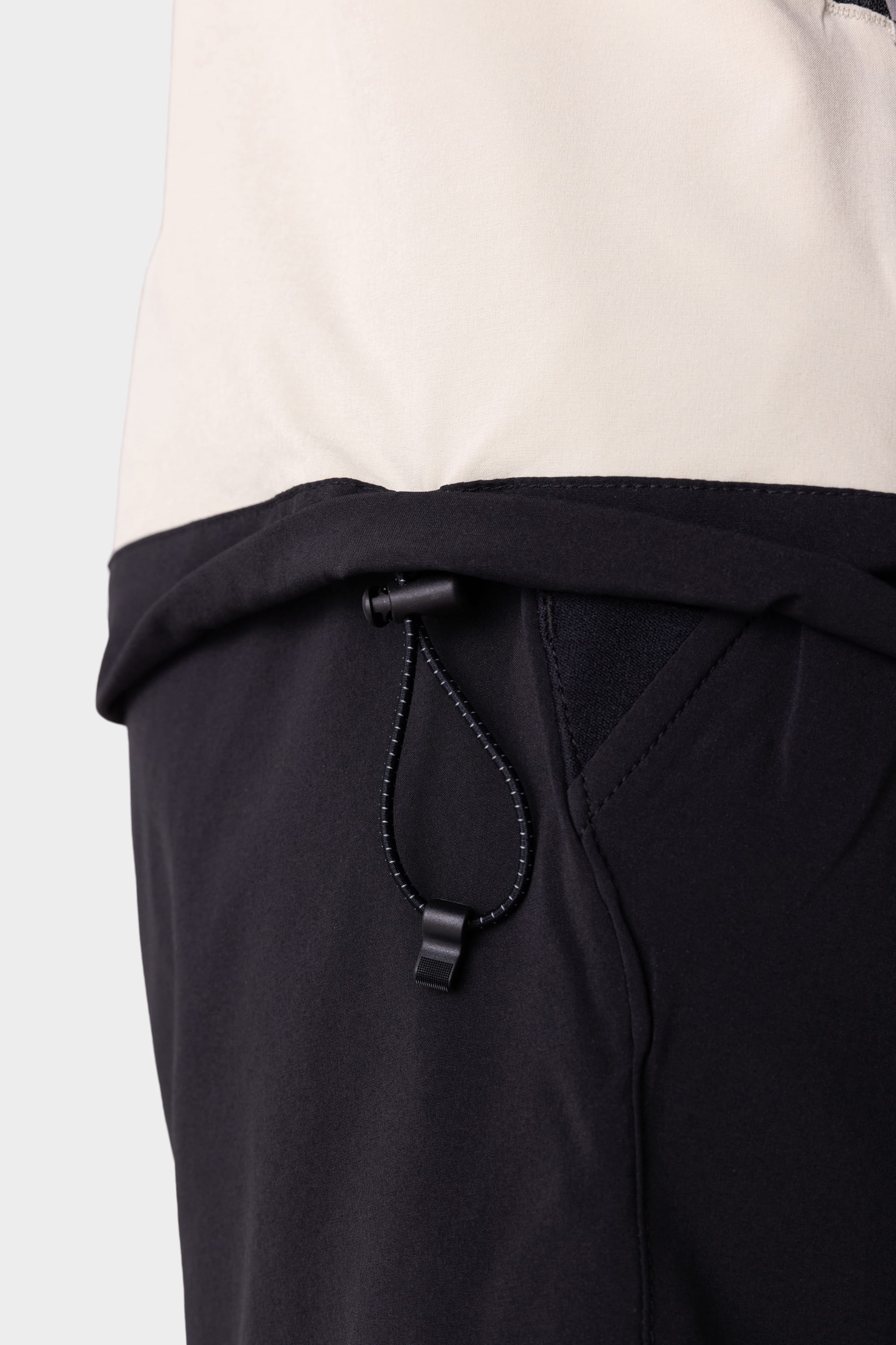 Close-up of the 686 Mens ATP Stretch Wind Jacket in black and beige, highlighting the side pocket area and adjustable elastic drawstring with plastic toggle.