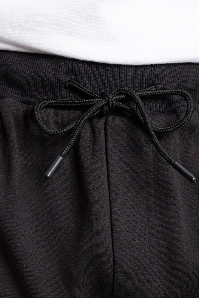 Close-up of the waistband on 686 Mens Everywhere Double Knit Short in black, featuring a black drawstring tied in a bow; a white shirt is partially visible at the top.