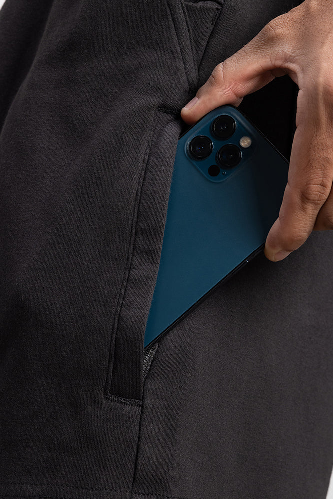 A hand slides a blue smartphone with three rear cameras into the pocket of dark pants: the 686 Mens Everywhere Double Knit Short by 686.