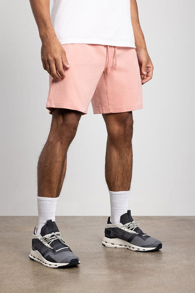 A person stands indoors wearing a white T-shirt, white crew socks, black athletic sneakers with white soles, and 686 Mens Everywhere Double Knit Short in light pink. The image is cropped at the torso to show only the lower body.