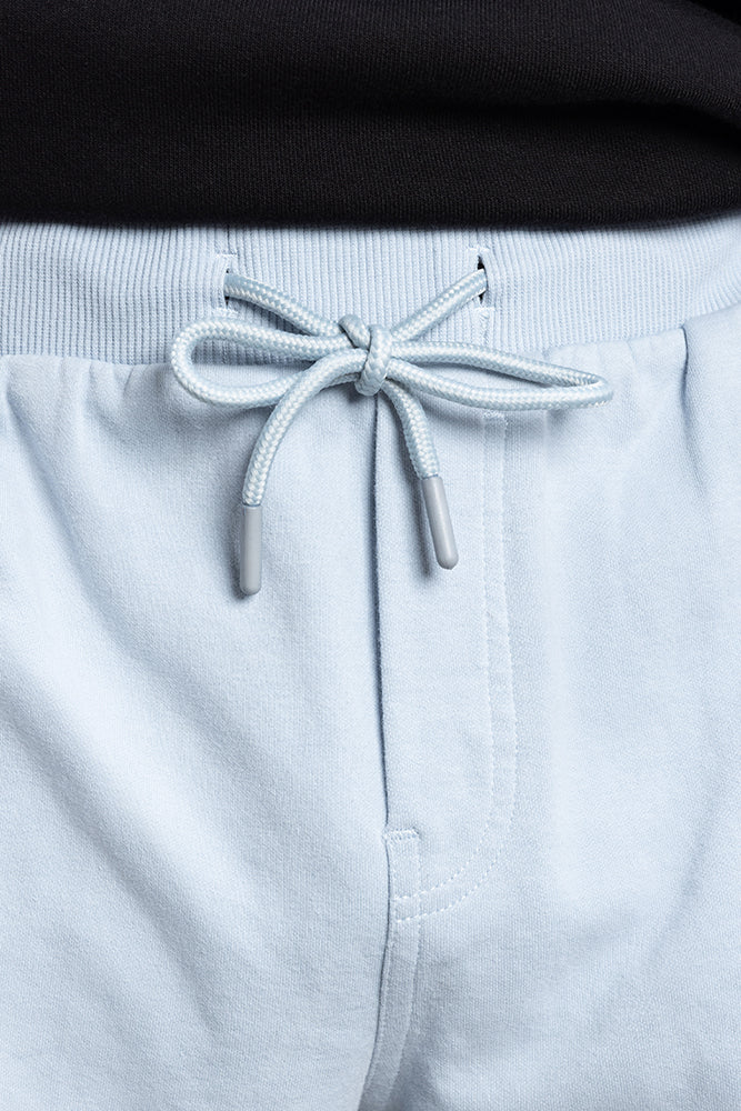 Close-up of a person wearing 686 Mens Everywhere Double Knit Shorts in light blue with a drawstring bow and a black shirt tucked into the waistband.