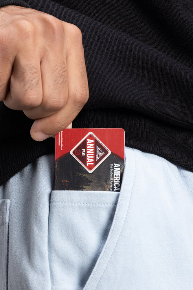 A person wearing a black top is placing a red and black annual pass card into the front pocket of light blue 686 Mens Everywhere Double Knit Shorts by 686.