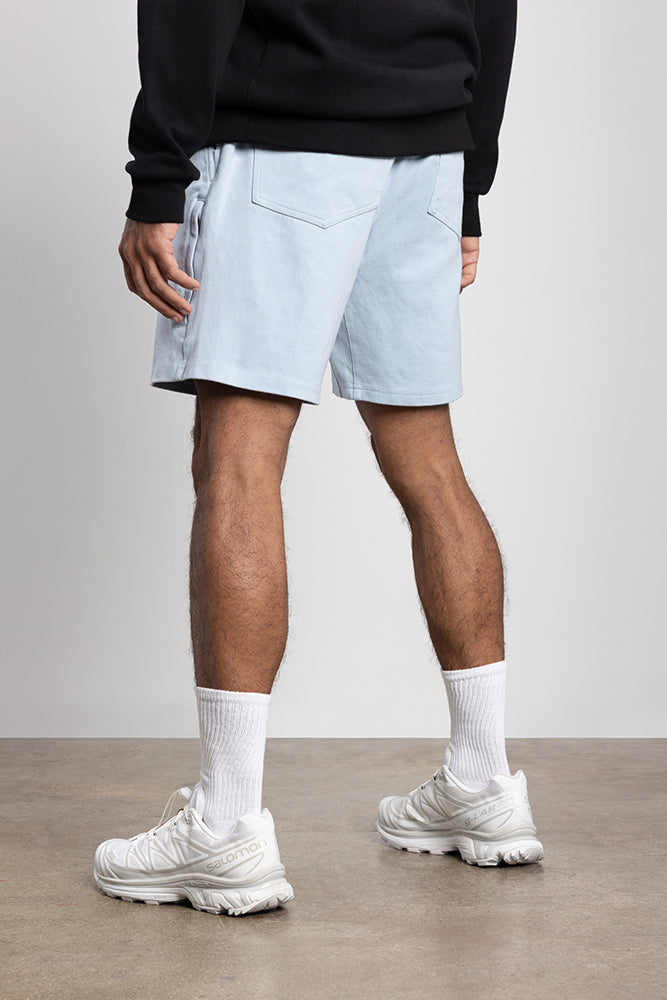 A person stands indoors on a smooth floor, wearing the 686 Mens Everywhere Double Knit Short in light blue, a black sweatshirt, white crew socks, and white sneakers. The photo is taken from behind, showing the outfit from waist down.